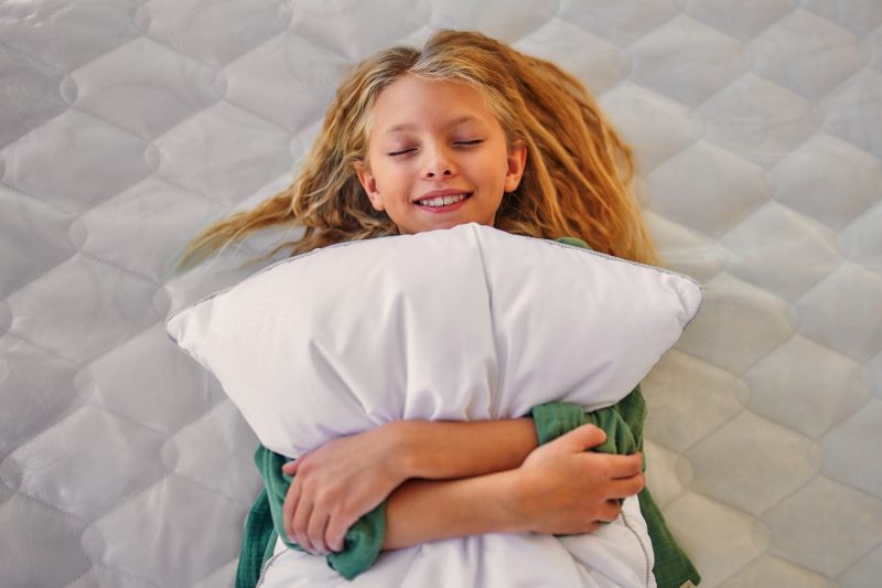 Una niña tumbada en la cama abrazada a la almohada.